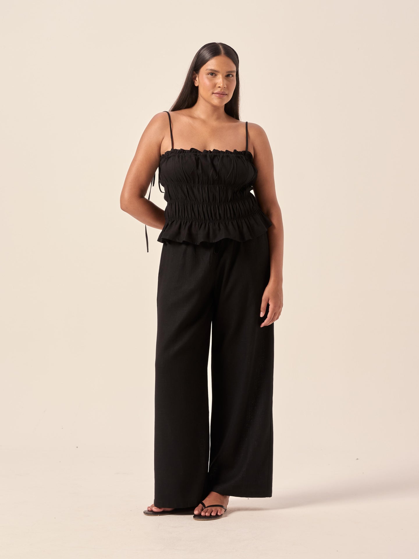 Woman wearing a black ruffled top and wide-leg pants on a beige background
