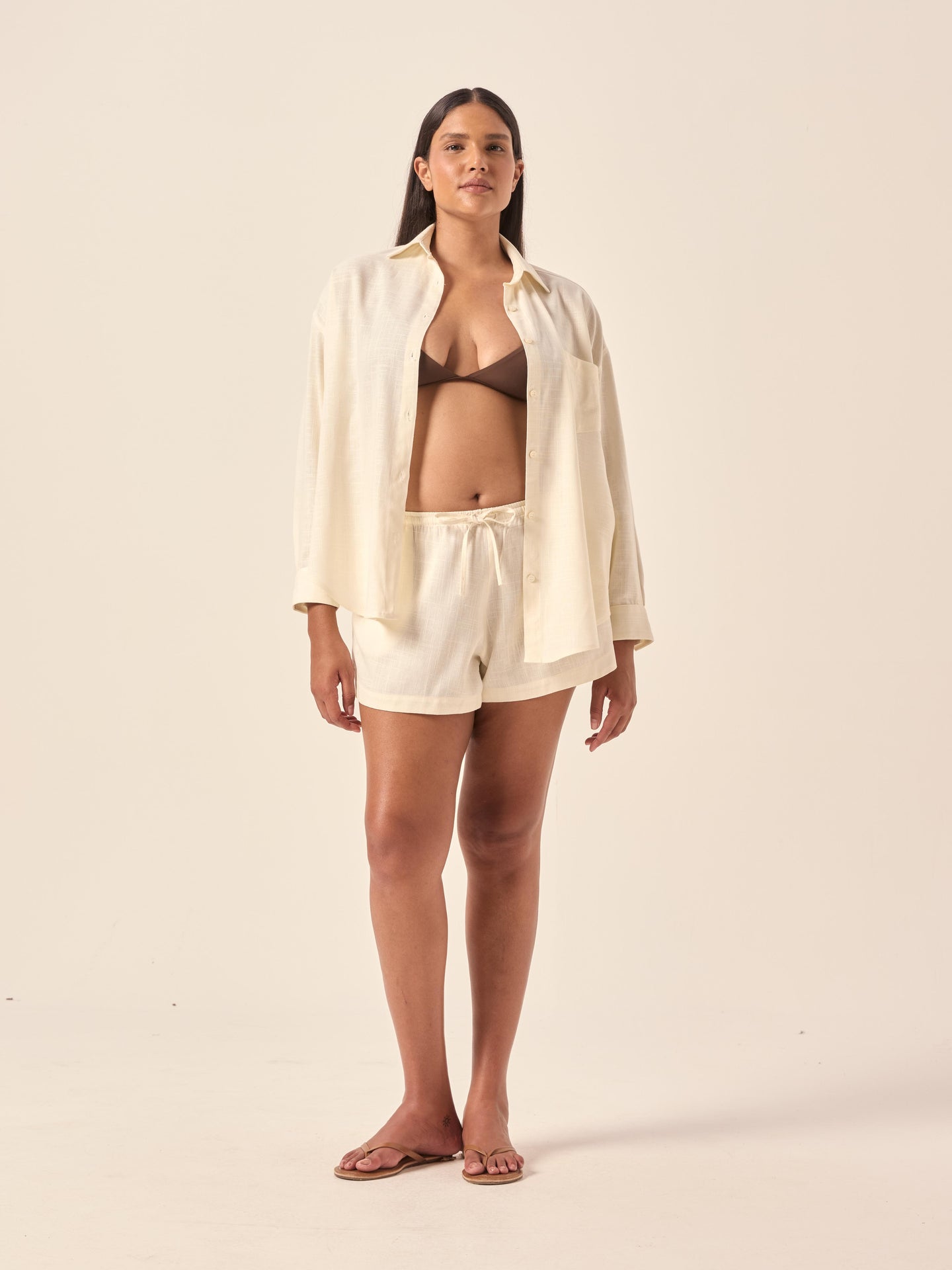 Woman wearing a beige shirt and white shorts on a plain background